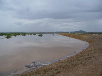 A large flooded area under a cloudy sky with distant hills.